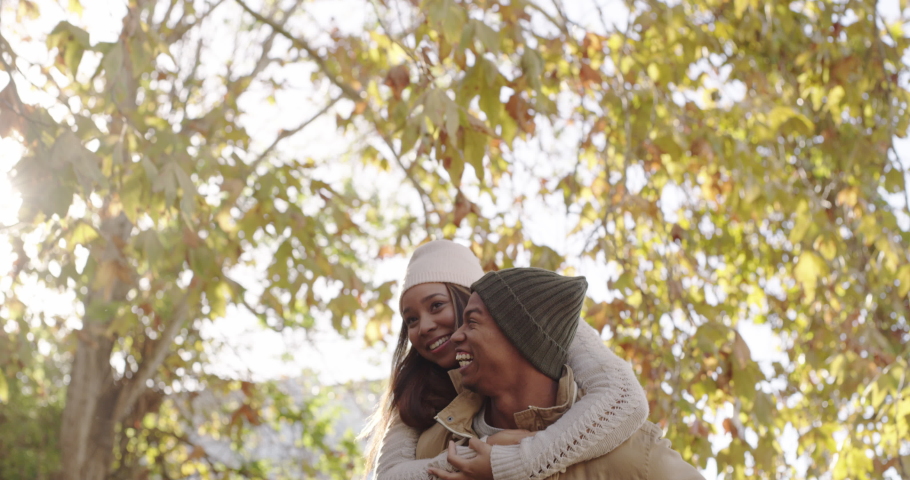 Loving, playful and happy couple having a piggyback and enjoying a fun date and walk through the park during autumn. Cheerful boyfriend laughing while giving his girlfriend a piggyback ride outdoors