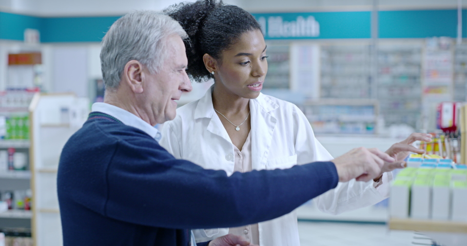 Friendly, helpful and experienced pharmacist assisting a senior customer with medication on a shelf in a pharmacy. African healthcare worker explaining dosage instructions to an elderly man Royalty-Free Stock Footage #1093176993