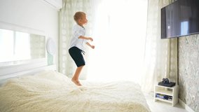 Caucasian baby boy jumping on parent's big bed indoor home in bedroom, looking at empty TV screen with copy space. Fun time at leisure activity. Happy childhood in motion. Cheerful happy moment life. - Powered by Shutterstock - Get 15% off with code: PIKWIZARD15