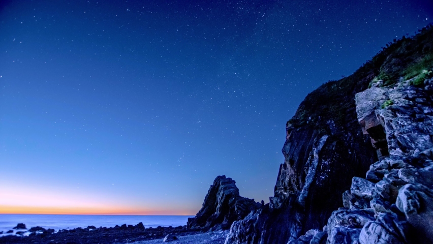 Star trails over the rocky beach on the coast of Devon, UK. 4K timelapse of the night sky shows the stars