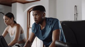 Fit Caucasian female cycling on stationary bike at an indoor fitness gym with group fitness class. Low angle pan up from feet to face. - Powered by Shutterstock - Get 15% off with code: PIKWIZARD15