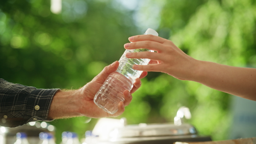 Close Up of a Anonymous Person Handing Over a Water Bottle to Another Person. Green Background in Nature. Outdoors Fourt Court Selling Drinks. Ecology, Healthcare and Hydration Concept.