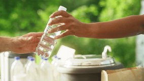 Close Up of an Anonymous Person Handing Over a Water Bottle to Another Person. Green Background in Nature. Outdoors Fourt Court Selling Drinks. Ecology, Healthcare and Hydration Concept. - Powered by Shutterstock - Get 15% off with code: PIKWIZARD15