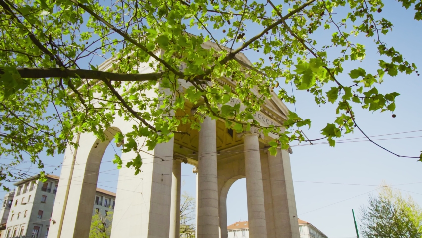 Green tree grows against old white arch in Ticinese on sunny day. Marble structure built in historical center of old city