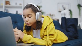 Black teenage girl in headphones listening to favorite song on laptop, music app