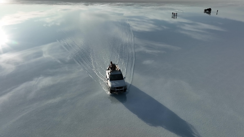 Uyuni, Salt flat Lake, Andes, Bolivia - March 2022:
Aerial fly drone view adventures Car 4x4 in in desolate Salar de Uyuni, in the middle and isolated world’s largest salt flat with reflections. 
