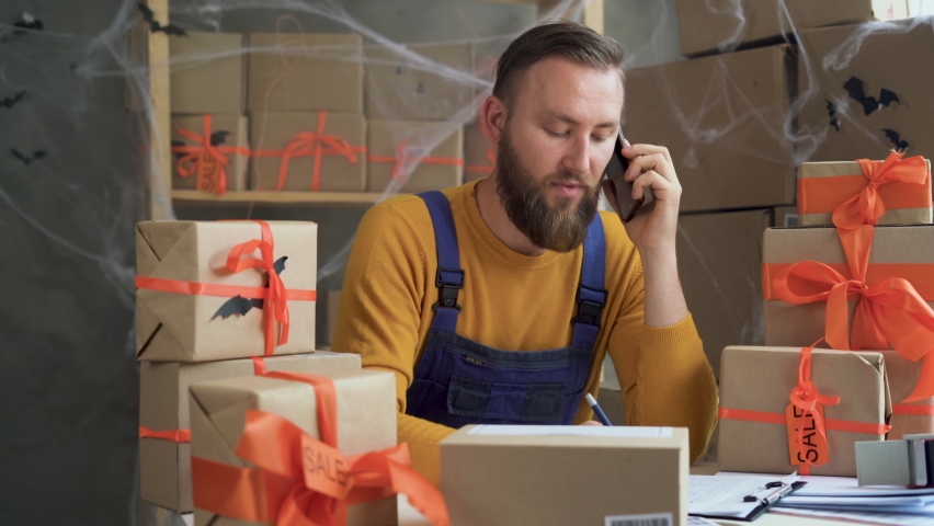 bearded man in glasses business owner sits in halloween decorated home office. takes orders online by phone. The concept of sale of goods holiday of all the dead, discounts and promotions.