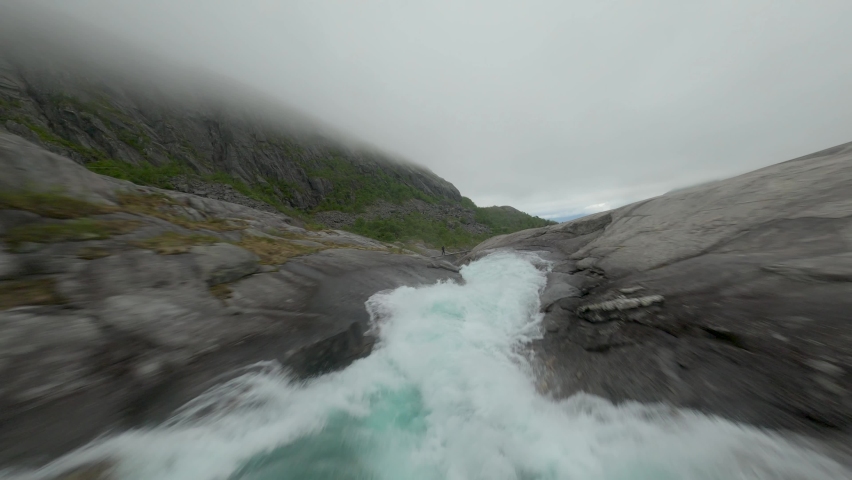 Fpv dynamic flight along waterfall under bridge in mountains of Norway during foggy sky - Spectacular drone footage of pilot