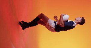 Vertical video of caucasian male rugby player running with rugby ball over pink lighting. Sport, movement, training and active lifestyle concept.