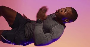 Vertical video of african american male runner with sportswear over pink lighting. Sport, movement, training and active lifestyle concept.