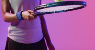 Video of midsection of african american female tennis player bouncing ball in neon pink lightning. Sport, movement, fitness and active lifestyle concept.