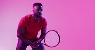 Video of focused african american male tennis player hitting ball on neon pink lightning. Sport, movement, training and active lifestyle concept.