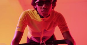 Video of focused african american female cyclist riding on neon orange lightning. Sport, movement, training and active lifestyle concept.