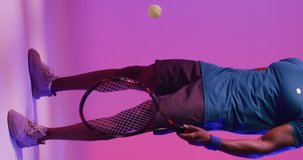 Vertical video of midsection of african american male tennis player bouncing ball on pink lightning. Sport, movement, training and active lifestyle concept.