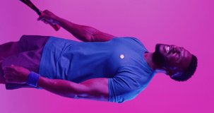 Vertical video of successful african american male tennis player on neon pink lightning. Sport, movement, training and active lifestyle concept.