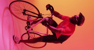 Vertical video of happy african american male cyclist riding on orange background. Professional sport, training and vintage style concept.