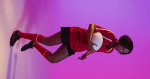 Vertical video of african american female rugby player running with ball over neon pink lighting. Sport, movement, training and active lifestyle concept.