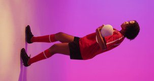 Vertical video of african american female rugby player running with ball over neon pink lighting. Sport, movement, training and active lifestyle concept.