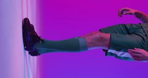 Vertical video of caucasian male soccer player with football over neon pink lighting. Sport, movement, training and active lifestyle concept.