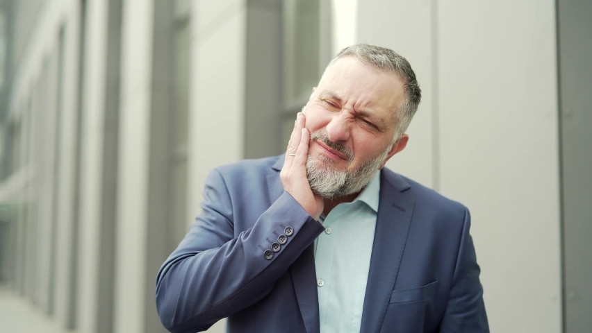 Mature business man with severe toothache standing on a city street near an office building. gray haired the employee having dental pain referred.diseases Standing front office building outside | Shutterstock HD Video #1093215563