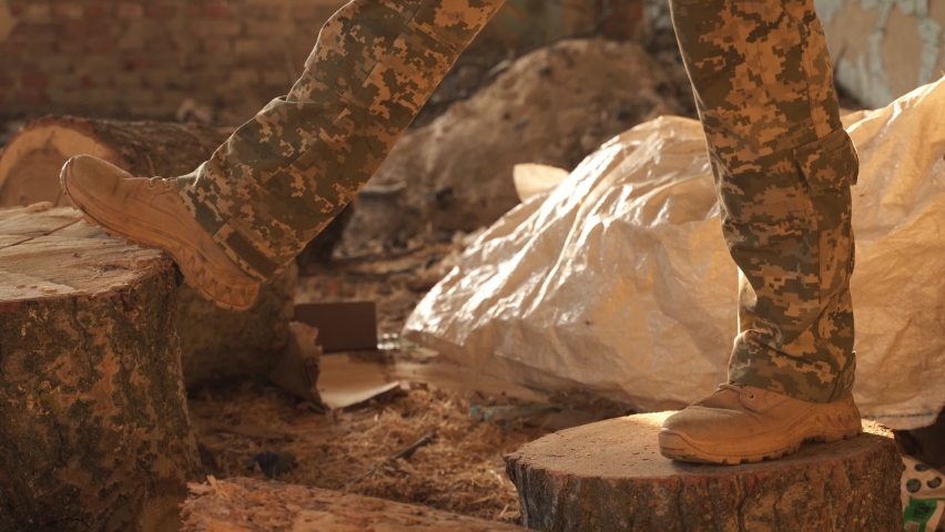 a soldier in camouflage pants and military boots stands on two wooden beams. harvesting firewood for heating by the military during the war. combat mission in winter.