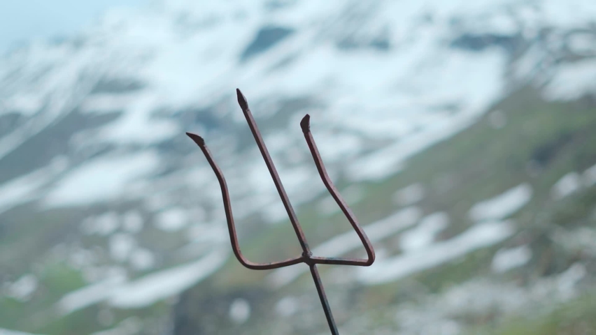 Close up shot of Shiva Trishul in background of snow Himalayan mountain at Rohtang pass at Manali, Himachal Pradesh, India. Trishul-Trident  of lord shiva in front of snow covered mountains | Shutterstock HD Video #1093216387