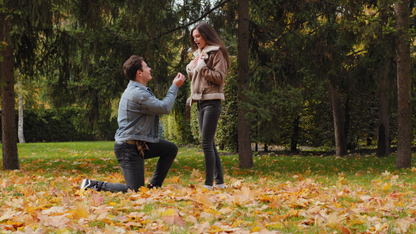 Confident young man stand on one knee in autumn park make marriage proposal to sweetheart caucasian beautiful girlfriend answering yes agree. Amazed woman embrace lovely guy outdoors love