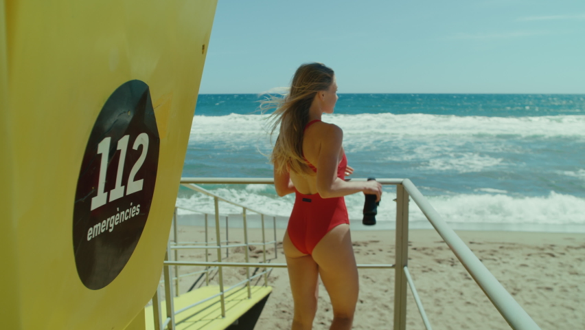 Young woman lifeguard on spanish beach look out through binoculars at sea. Bay watch concept, safety in open waters, safe vacation during storm. Sign says 112 emergency services in spanish Royalty-Free Stock Footage #1093217821