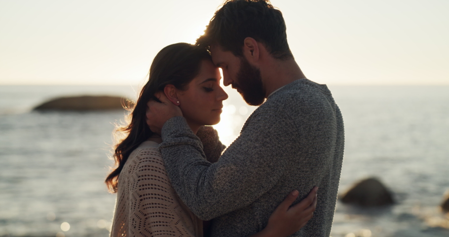 Romantic, happy and hugging young couple sharing a beautiful moment on a beach sunset date. In love partners enjoying romance by the ocean. Carefree people loving the sea and outdoors together