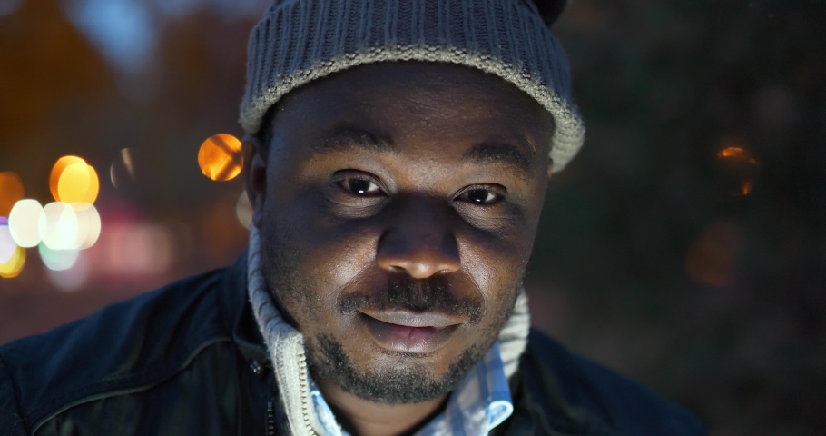 Cheerful african american man in winter hat looks at the camera and smiles shyly, close-up shot Royalty-Free Stock Footage #1093219359