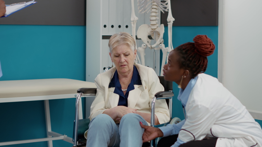Nurse and doctor consulting woman with chronic impairment, doing physiotherapy examination in cabinet. Senior adult wheelchair user receiving alternative medicine consultation. | Shutterstock HD Video #1093219437