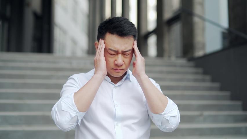 exhausted young asian business man office worker stand outdoors. stressed overworked male with a severe headache massages head. Depressed Tired employee suffering pain sick work outside Royalty-Free Stock Footage #1093220061