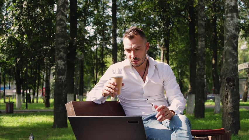Handsome man - white collar, talking online and gesturing with his hands. Young man in a city park, hot sunny summer day. Warm soft light, close-up. Against the background of green trees. 4K UHD. | Shutterstock HD Video #1093222557