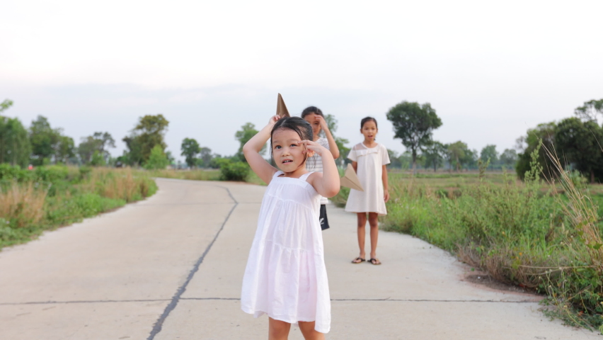 Asian little girl running and playing with paper plane toy with her siblings. Group of asian kids running and playing together in the rural street with fun. Slow motion shot. Royalty-Free Stock Footage #1093226409