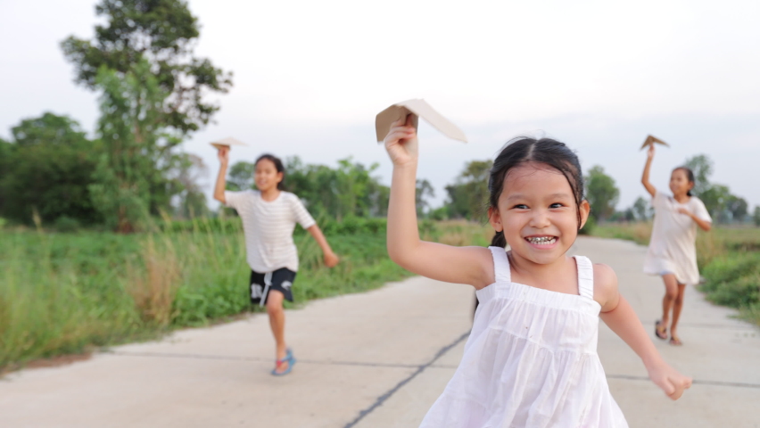 Asian little girl running and playing with paper plane toy with her siblings. Group of asian kids running and playing together in the rural street with fun. Slow motion shot. Royalty-Free Stock Footage #1093226409