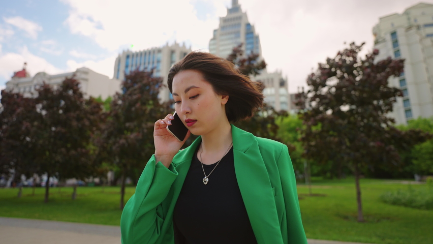 young chinese businesswoman is talking by cell phone walking in downtown in big city