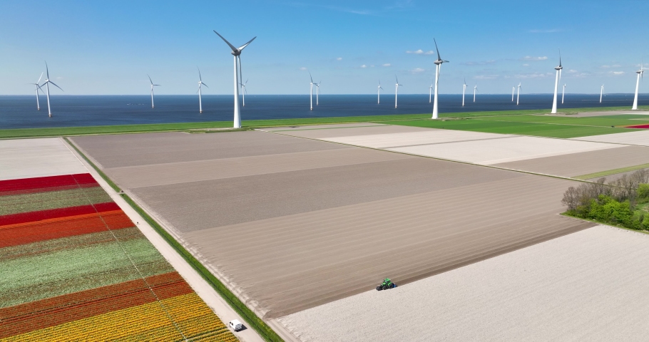 Aerial 5K view of farmland with a running tractor, tulip field and wind farm along IJsselmeer dike, Noordoostpolder, Flevoland, Netherlands. | Shutterstock HD Video #1093229177