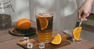 4k video, drinking fresh blending black coffee Arabica with orange juice for health care drinking in home or cafe. woman used hand take orange slices fruit into cup with orange mixed espresso short