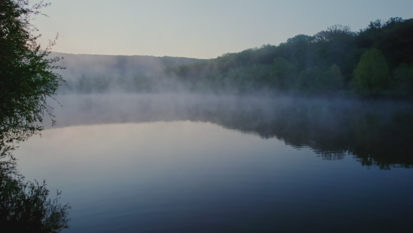 Close-up over water drone footage of the evaporation process before sunrise, above a la in the forest. Aerial shot shot with a drone. Royalty-Free Stock Footage #1093241289