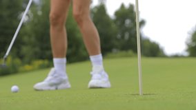 Woman golfer hit ball with club and striking into hole on green course