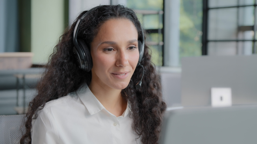 Latino arabian positive woman in headphones communicates via video call center operator talks to customer on online conference webcam on computer talking using headset distance office chat e-learning Royalty-Free Stock Footage #1093249921
