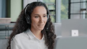 Latino arabian positive woman in headphones communicates via video call center operator talks to customer on online conference webcam on computer talking using headset distance office chat e-learning