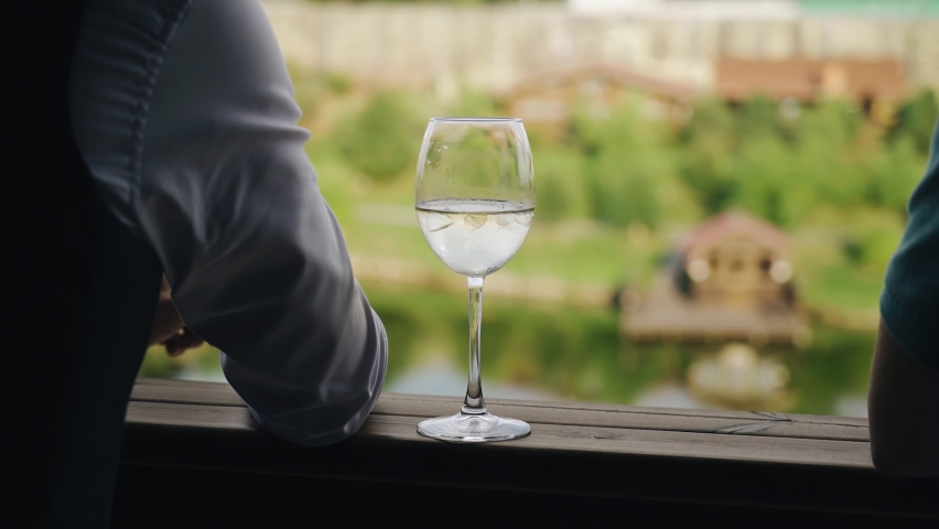 A man smokes on the balcony and next to him on the railing is a glass of wine. Serene atmosphere of relaxation