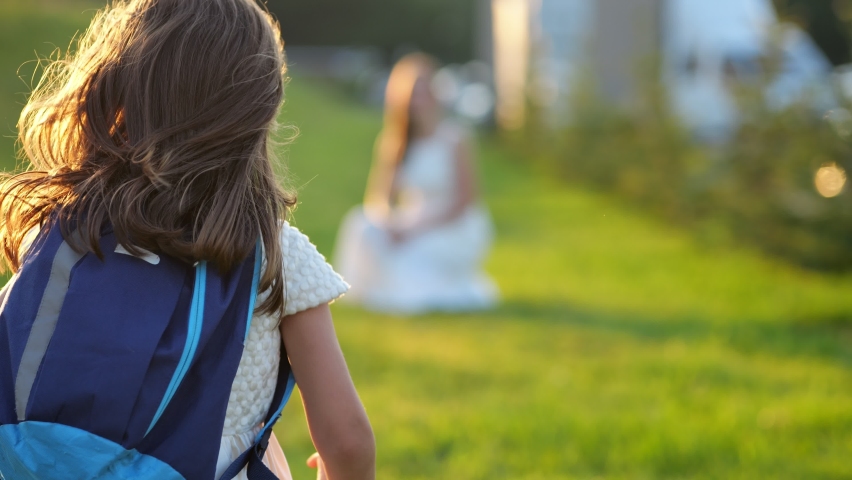 Happy girl with blue schoolbag runs and hugs mother. Parent kisses excited daughter and interested about first day at elementary school at sunset Royalty-Free Stock Footage #1093271707