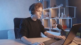 The blogger plays during the stream, listens to music and dances with his head. Curly, dark-haired guy. Vlogger, streamer. Young man. Handsome guy. Headphones.