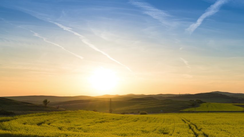 A large spring flowering field with bright yellow small plants in a mountain and meadow valley against the backdrop of a golden evening sunset sky, in warm country of Bulgaria. 4K UHD timelapse
