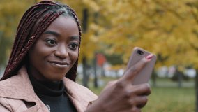 Close-up young happy woman standing in autumn park communicates video chat on smartphone friendly online conversation joyful smiling girl talking with friend on webcam on phone answering video call