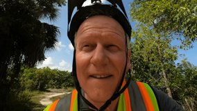 Wide-angle closeup tracking with middle-aged cyclist traveling along a trail through trees with bumps in slow motion in a sunny afternoon at Quiet Waters Park in Deerfield Beach, Florida