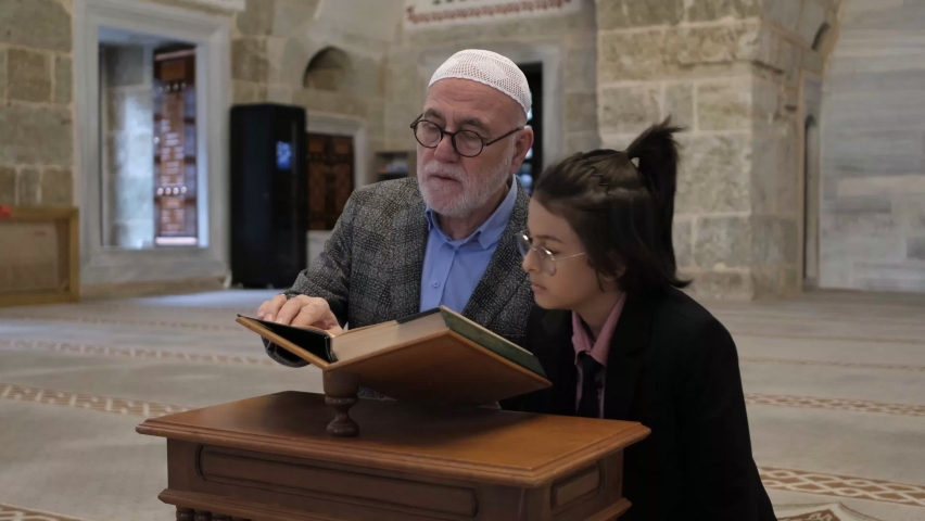 Grandfather teaching his granddaughter to recite the Quran in the mosque, the image of the boy taking the Quran reading lesson on the wooden lectern