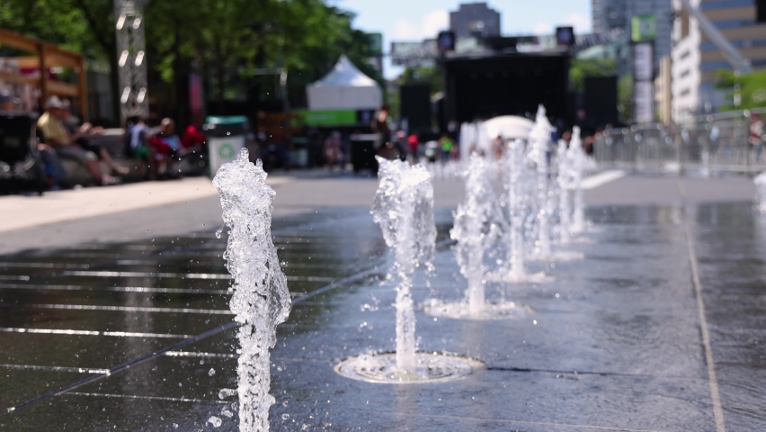 Slow mo selective focus clip of splash fountain water jets spraying out of sidewalk in city center of Montreal, Canada during summer. With copy space.